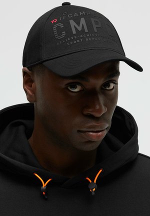 Schwarze Kappe mit erhabenen Buchstaben "CMPD" und roten Akzenten. Weicher Stoff, gebogener Schirm, kombiniert mit einem schwarzen Hoodie mit orangefarbenen Kordeln.