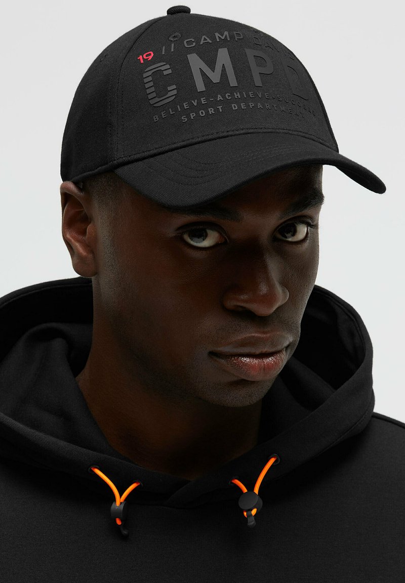 Black cap with raised text "CMPD" and red accents. Soft fabric, curved visor, paired with a black hoodie featuring orange drawstrings.