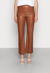 Bruine faux leren flared broek met een hoge taille, een gladde textuur en een strakke uitstraling. Draagt met witte gespsandalen met hakken.