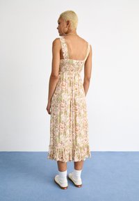 Bloemrijke midi-jurk in lichtroze en groen, met een smock achterzijde, brede banden en een rucheszoom. Gestyled met witte sokken en schoenen.