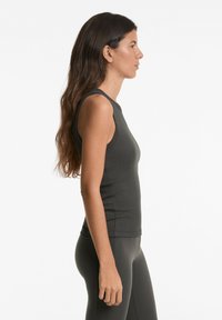 Top senza maniche grigio scuro con texture a coste e design aderente, caratterizzato da un collo rotondo e orlo dritto, indossato con leggings abbinati.