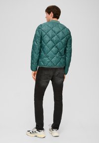 Tükisfarbene Steppjacke mit Rautenmuster, mit rundem Kragen und geripptem Saum, kombiniert mit schwarzen Skinny-Jeans und grauen Sportschuhen.