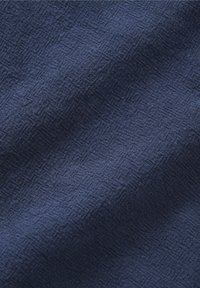 Gros plan d'un tissu bleu foncé avec un motif texturé subtil et des détails de tissage visibles.