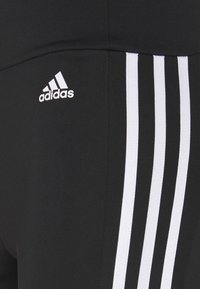 Svarta träningsleggings med vita tre-strimmor, med en liten vit Adidas-logga på  övre vänstra sidan. Slät textur.