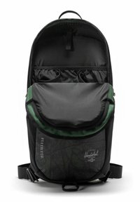 Sac à dos noir avec un rabat vert, présentant un design texturé, plusieurs poches intérieures et une poignée supérieure. Bretelles ajustables incluses.