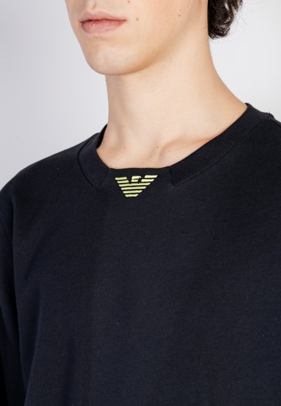 T-shirt nera in cotone con scollo rotondo. Presenta un piccolo logo a righe gialle sul colletto. Texture liscia, design casual.