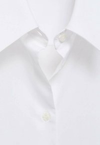Gros plan sur le col d'une chemise blanche et la patte de boutonnage avec deux boutons blancs visibles.