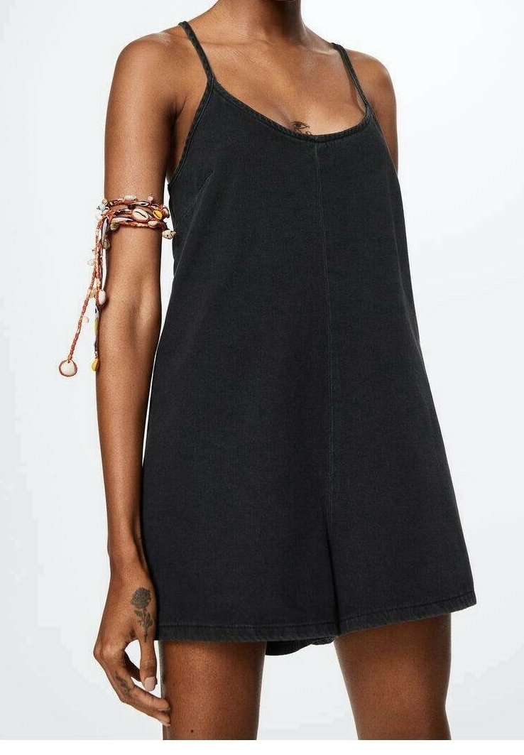 Vestido de mezclilla negra con tirantes finos, corte relajado y escote redondeado. Presenta costuras mínimas y una pulsera intrincada en el brazo.