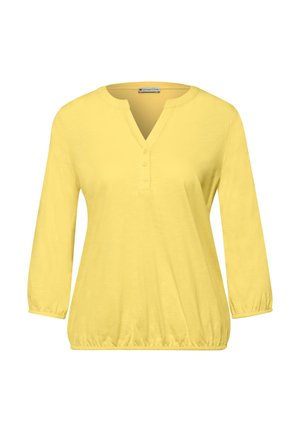 Gul langærmet bluse til kvinder med tre-knaps V-hals samt elastiske manchetter og kant.