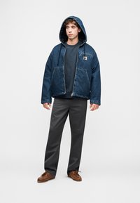 Τζι ν μπουφάν με κουκούλα και δύο εμπρόσθιες τσέπες, σε συνδυασμό με πουκάμισο σκούρου μπλε και γκρι παντελόνι. Καφέ παπούτσια με κορδόνια ολοκληρώνουν την εμφάνιση.