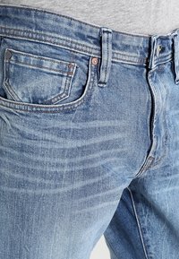 Bleděmodré džíny z denimu s klasickým střihem, předními a zadními kapsami a kontrastním prošitím podél švů.