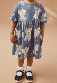Baumwollkleid mit kurzen Ärmeln, blauer Hintergrund und Feenmotiven. Hat eine geraffte Taille und wird mit weißen Rüschenstrümpfen und marineblauen Schuhen kombiniert.