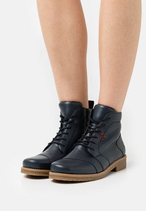 Bottines en cuir bleu marine avec un bout rond, laçage à l'avant, coutures décoratives rouges et semelle en caoutchouc. Accents texturés près de la cheville.