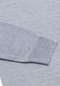 Világosszürke, hosszú ujjú textil, bordás mandzsettával és puha, sima felülettel; egyszínű dizájn, látható minták vagy kiegészítők nélkül.