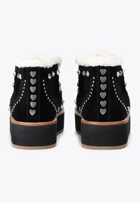 Czarne zamszowe botki za kostkę z puszystym białym wykończeniem, ozdobione srebrnymi ćwiekami i sercowymi akcentami wzdłuż boków i z tyłu.