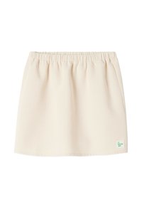 Jupe mini beige clair avec une taille élastique, fabriquée à partir d'un tissu doux, dotée d'une petite étiquette de marque verte en bas à droite.