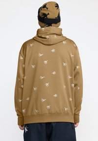 Un sweat à capuche marron avec un motif de oiseaux blancs répété, doté d'une capuche à cordon de serrage et d'un ourlet côtelé. Accompagné d'un bonnet beige avec des accents noirs.