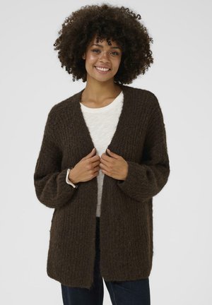 Brown knitted cardigan with a loose fit, ribbed texture, and open front design. Long sleeves and worn over a light-colored top.