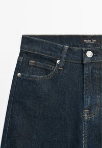 Section taille d'un jean en denim bleu foncé avec poche avant, bouton argenté, passants de ceinture et étiquette noire Massimo Dutti.