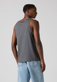 Débardeur gris en tissu doux, avec un col arrondi et sans manches. Associé à un jean bleu clair à coupe décontractée.