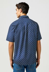 Camisa de manga corta azul marino con un patrón floral en blanco, con cuello abotonado y diseño de yugo trasero para un ajuste ajustado.