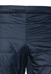 Marinblå isolerade byxor med en kviltad design, som har horisontell sömnad och en mjuk textur. Inkluderar en sidöppning.