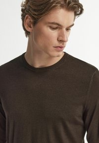 Brun stickad tröja med rund halsringning och långa ärmar, med en slät yta och diskreta söm detaljer.