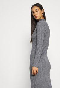 Graues, geripptes Strickkleid mit langem Ärmel und hohem Kragen, das eine taillierte Silhouette hat, die an der Taille und an den Hüften schmaler wird.