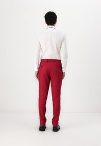 Pantaloni din in roșu, cu croială slim, cu două buzunare la spate și o textură netedă, asortați cu o cămașă albă cu mânecă lungă.