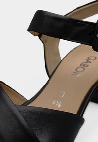 Μαύρο δερμάτινο σανδάλι με φαρδιά λουρί και αγκράφα αστραγάλου. Διαθέτει λεία υφή, επενδεδυμένο πάτο και τυπωμένες λεπτομέρειες μεγέθους.