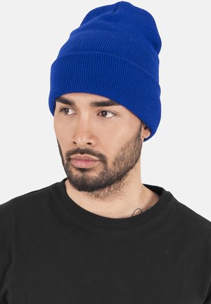 Blå strikket hue med ribbet tekstur og ombukket kant. Bæres sammen med en sort crew-neck t-shirt med korte ærmer og en glat overflade.