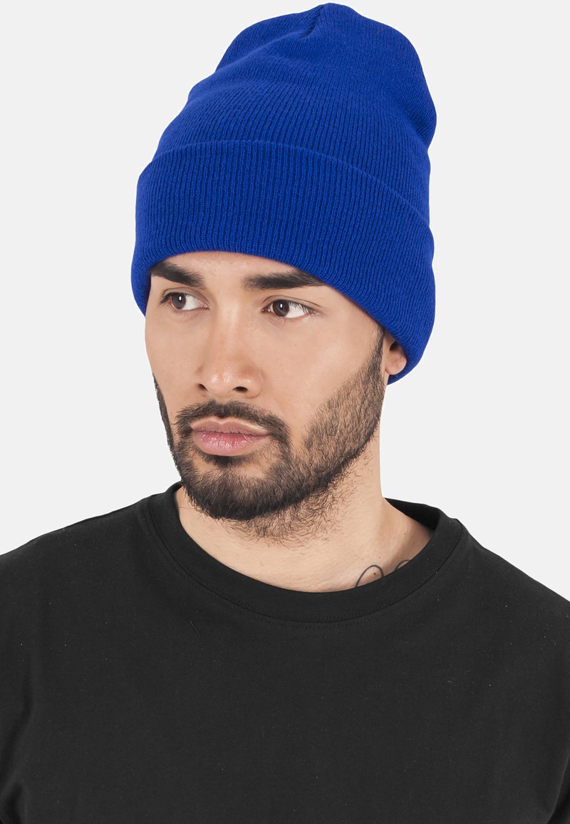 Căciulă tricotată albastră cu o textură ribbată și o margine rimbată. Pur tată cu un tricou negru cu guler rotund, având mâneci scurte și un finisaj neted.