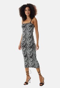 Black and white zebra print midi dress with thin straps, fitted design, and a smooth texture. Paired with black strappy high-heeled sandals.