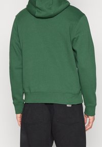 Grön huvtröja med en strukturerad tyg och huva. Baksidan har en ribbad fåll och manschetter. Buren med svarta byxor med avslappnad passform.