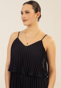 Vestido plisado oscuro en azul marino con un diseño en capas, que cuenta con tirantes de spaghetti ajustables y una textura suave. Se pueden ver collares de oro en capas.
