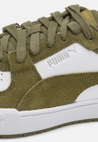 Olive green suede sneaker with white leather accents, textured laces, and a white rubber sole. Features embossed logo detail.