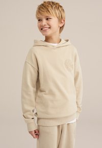 Beige Kapuzenpullover mit gerippten Bündchen und einem Logo auf der Brust. Weicher Stoff mit einer lockeren Passform, getragen mit passenden beigen Hosen.