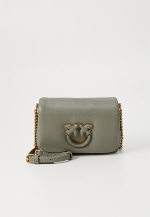 Zelena kožnata torbica s zlatnim lancem, koja na prednjoj strani ima grb s dva lista i smiješak, te glatku, mat teksturu.