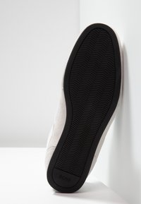 Idrottssko med övre i grå mocka och en strukturerad svart gummisula, med logotyp på hälen och en slät design.