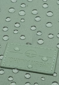 Vízálló, menta zöld szövet, kiemelkedő pöttyökkel és vízcseppekkel; a felszíne texturált, és egy varrott címke található rajta, melyen a "JOHNNY URBAN" felirat olvasható.