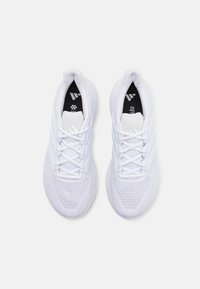 Des chaussures de sport blanches présentent un dessus en maille respirante, un col rembourré et des lacets plats. Un design notable à trois bandes sur les côtés.