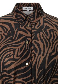 Braun und schwarzes Zebra-Print-Shirt mit Kragen und goldenen Knöpfen, das über eine elegante Stoffstruktur und auffällige Muster verfügt.