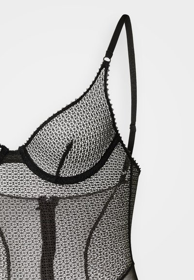 Černý krajkový body s geometrickým síťovaným vzorem, nastavitelnými ramínky a vroubkovanými okraji podél výstřihu a lemů.