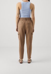 Hnědé cargo kalhoty s elastickým pasem, bočními kapsami a elegantním designem, zkombinované se světle modrým žebrovaným tílkem, pohled zezadu.