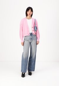Rosa strikket cardigan med treknapper, hvit t-skjorte, lyseblå vidde jeans med frontbroderi, og svarte ankelstøvler med stjernedetaljer.