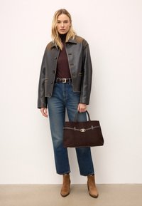 Svart konstläderjacka med guldaccenter, vinröd polotröja, blå högmidjade jeans, bruna mockaankelboots och en mörkbrun handväska.