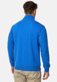 Blå fleecepullover med høj krave, lange ærmer samt ribstrik ved håndled og kant. Glat tekstur og afslappet design, velegnet til lag-på-lag.