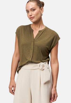 Camicia verde oliva con maniche a cappuccio e bottoni, con colletto, abbinata a pantaloni larghi color crema con dettaglio in vita annodato. Texture liscia.
