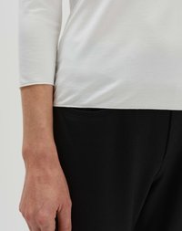 T-shirt blanc à manches longues avec une texture lisse, associé à un pantalon noir avec un détail de poche subtil. Accent sur des couleurs neutres et un ajustement confortable.