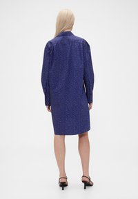 Blue polka dot shirt dress, lightweight fabric, long sleeves, collar, knee-length hem, with button details on sleeves and back.